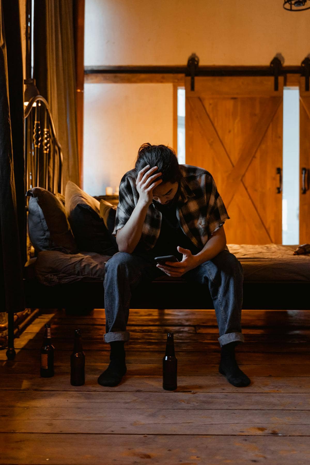 Jeune homme assis seul dans une pièce sombre, tenant son téléphone, l'air épuisé — stress et réflexe porno